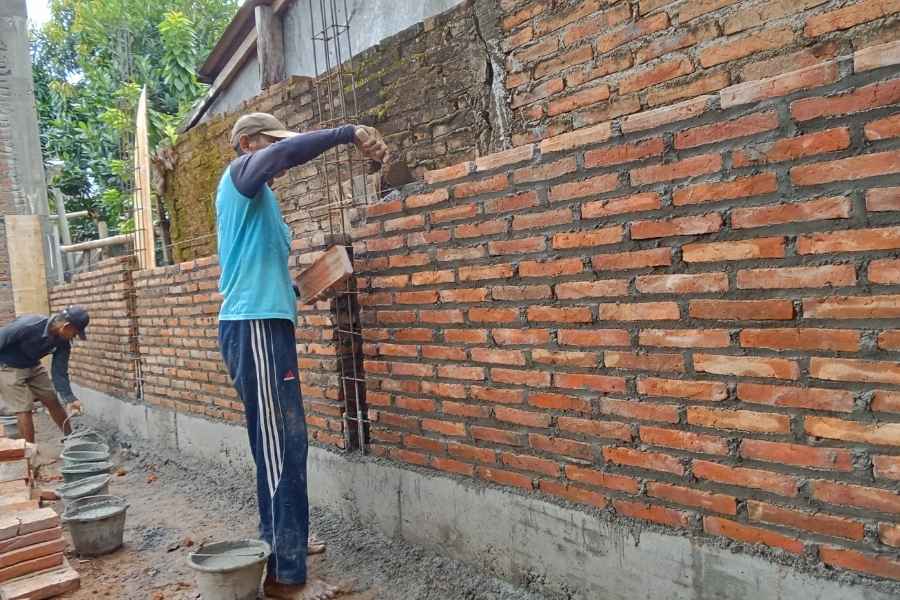 Two workers laying a masonry brick wall on an outdoor construction site.