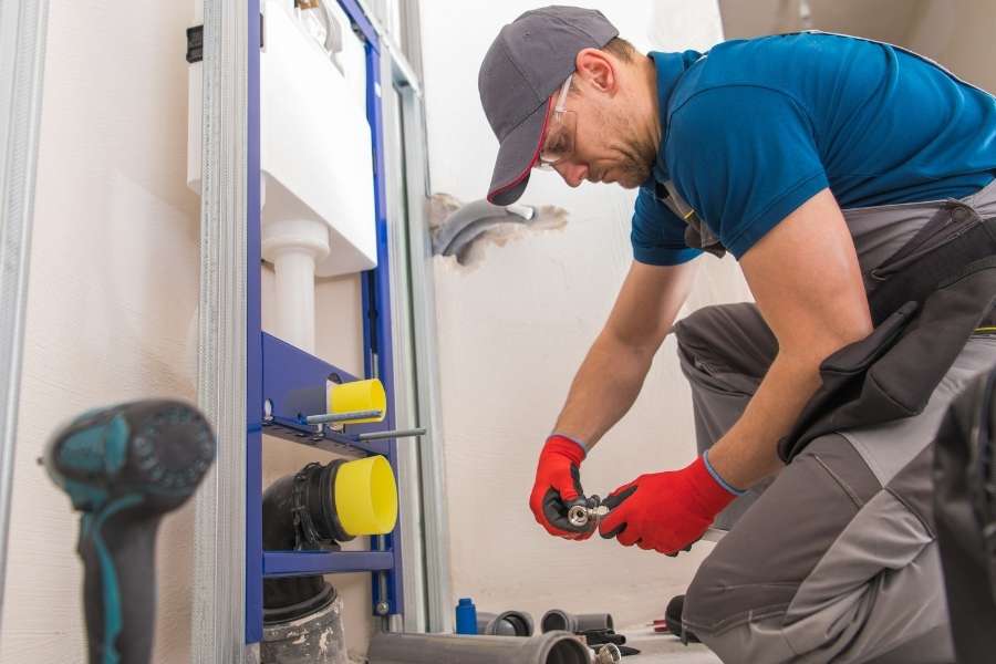 A plumber kneeling down and fitting small components for a home plumbing system.